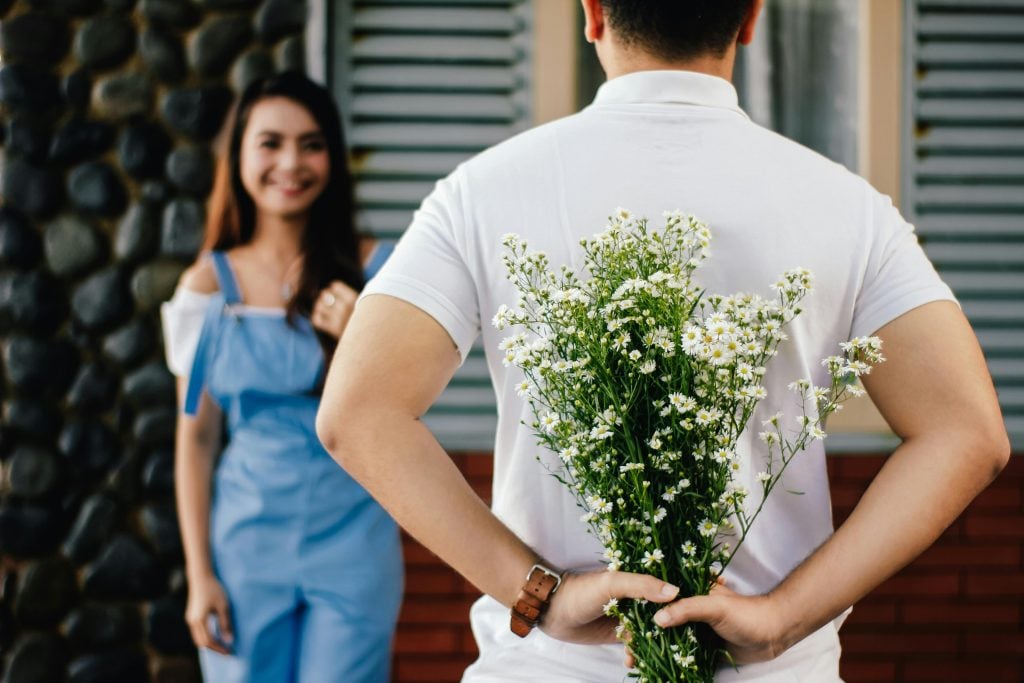 Homem escondendo buquê de flores de mulher